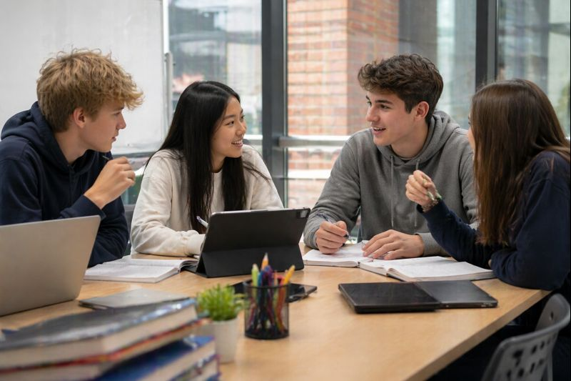 High school students collaborating around a table with laptops and notebooks